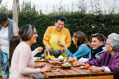 Latin x family sitting around an outdoor table eating dinner