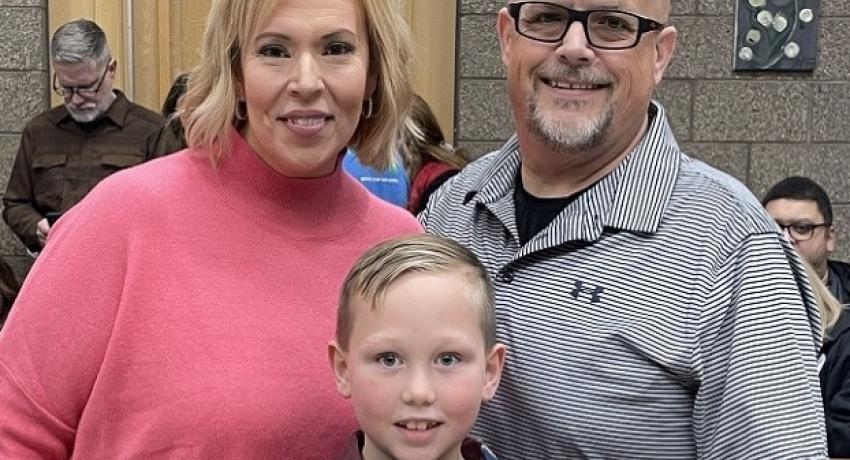 Two parents stand behind one male child smiling 