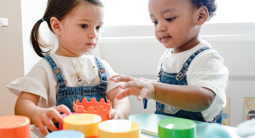 Boy of color with dark hair plays with colorful blocks with girl with brown hair.