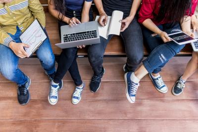 Youth sitting on bench with computers and book.