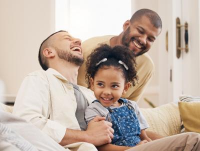 Two fathers and child sitting on a couch laughing
