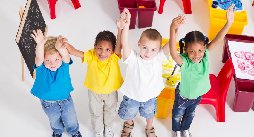Four young children at school raising their hands together