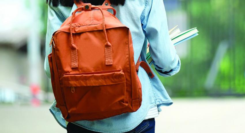 Girl walking to school with backpack and books in her arms.