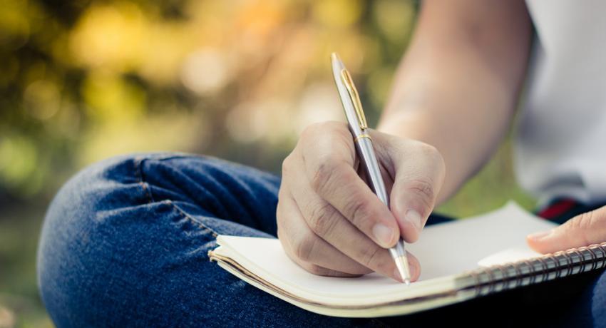 A young person writing in a journal outdoors. 