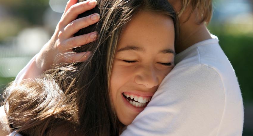 Child smiling while hugging caregiver. 