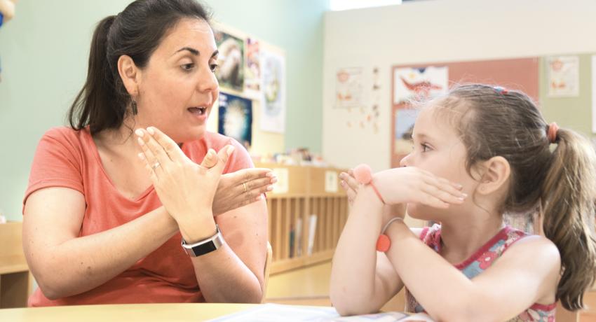 Female teacher and young female child practice American Sign Language (ASL).