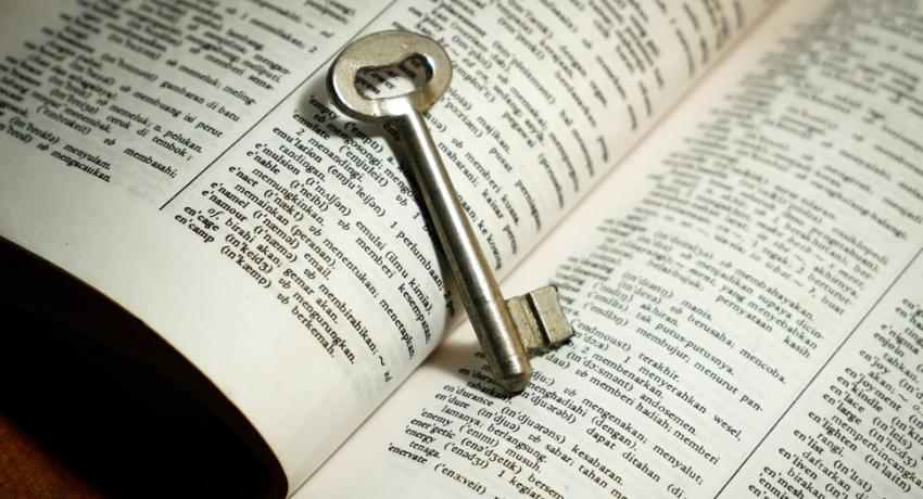 Open dictionary laying on a table with an old-fashion skeleton key laying across the fold. 