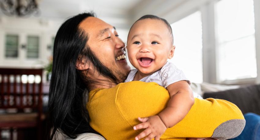 Man of color in yellow shirt holds smiling toddler in his arms