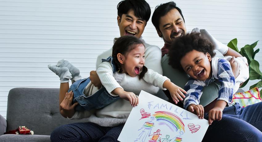 Adoptive family with two kids, two parents, drawing family picture, sitting on sofa in living room at home. 