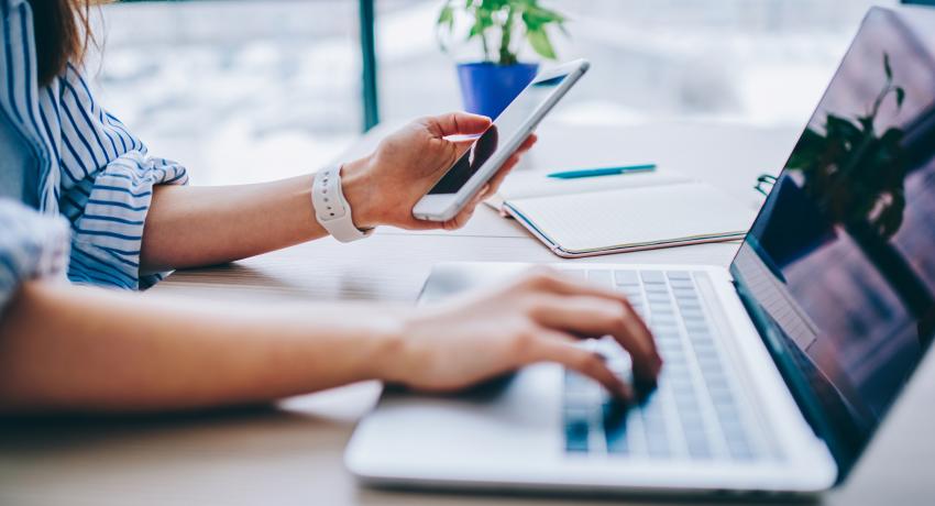 photo of a person's arms with a phone and computer at a desk