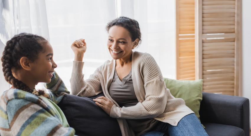 one parent with a teen, sitting on chairs facing each other, smiling. 