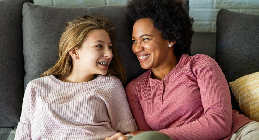 Teen girl and adult woman itting on couch and smiling at each other