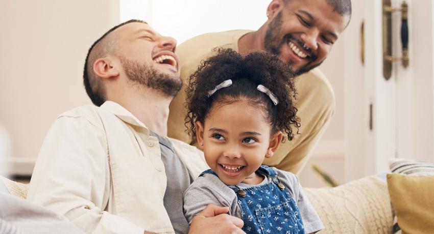 Two fathers and child sitting on a couch laughing